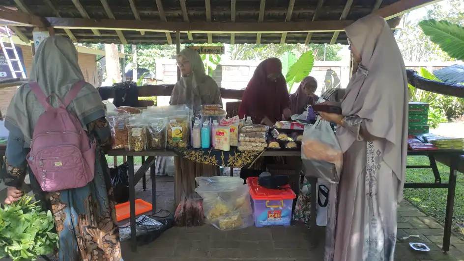 Beberapa perempuan berhijab bertransaksi di lapak bazar UMKM yang menjual aneka makanan kemasan di bawah bangunan semi terbuka.